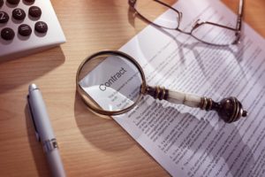 A magnifying glass is laid on top of a merchant processing contract representing how you need to review the fine print when selecting a merchant processor for your business.